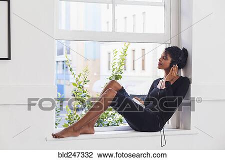 Mixed Race woman sitting in windowsill listening to headphones View Large Photo Image Stock Image - Mixed Race woman sitting in windowsill listening to headphones. Fotosearch
