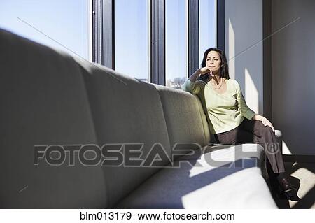Stock Photo - Mixed race woman sitting on bench in lobby. Fotosearch