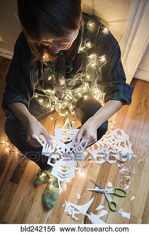 Stock Photograph - Mixed Race woman sitting on floor wrapped in string lights holding snowflake. Fotosearch