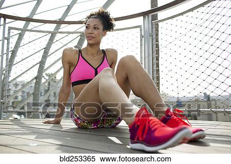 Stock Photography - Mixed Race woman sitting on wooden floor near fence. Fotosearch