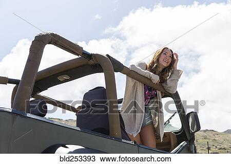 Stock Image - Mixed Race woman standing in convertible car. Fotosearch