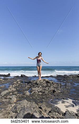 Stock Image - Mixed Race woman standing on rocks on beach. Fotosearch
