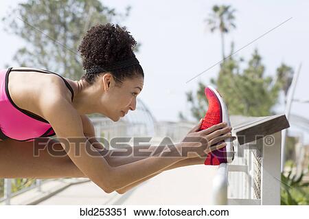 Stock Image - Mixed Race woman stretching leg on banister. Fotosearch