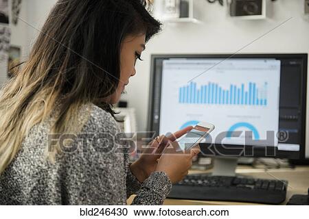 Mixed Race woman texting on cell phone near computer View Large Photo Image Stock Image - Mixed Race woman texting on cell phone near computer. Fotosearch