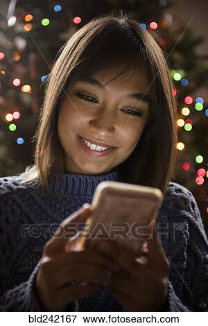 Stock Photo - Mixed Race woman texting on cell phone near Christmas tree. Fotosearch