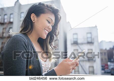 Stock Photograph - Mixed Race woman texting on cell phone in city. Fotosearch