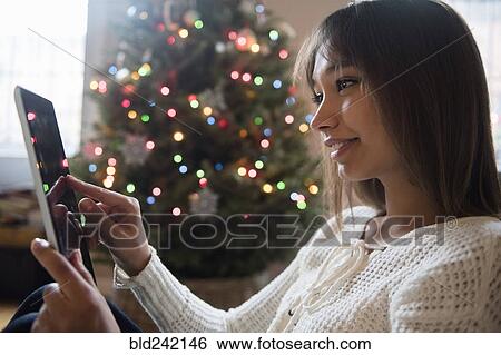 Mixed Race woman using digital tablet near Christmas tree View Large Photo Image Stock Photograph - Mixed Race woman using digital tablet near Christmas tree. Fotosearch