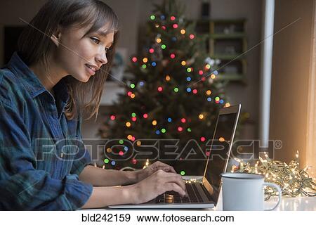 Mixed Race woman using laptop near Christmas tree View Large Photo Image Stock Photo - Mixed Race woman using laptop near Christmas tree. Fotosearch
