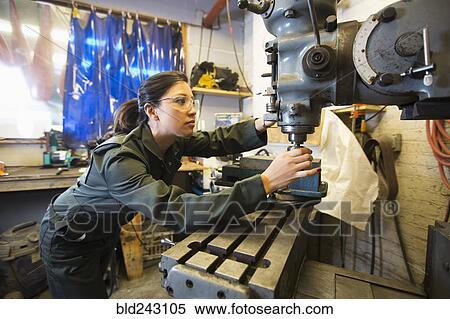 Stock Photography - Mixed Race woman using machinery in workshop. Fotosearch