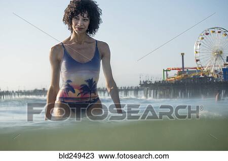 Stock Image - Mixed Race woman wading in ocean near amusement park. Fotosearch