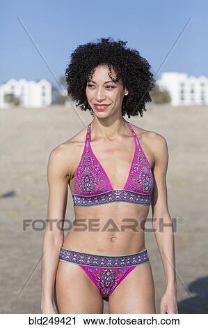 Stock Image - Mixed Race woman wearing bikini standing on beach. Fotosearch