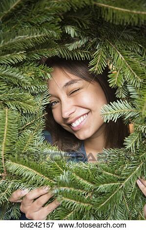 Mixed Race woman winking in pine wreath View Large Photo Image Stock Photo - Mixed Race woman winking in pine wreath. Fotosearch