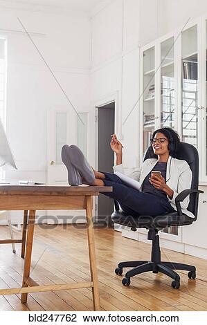 Mixed Race woman with feet up listening to cell phone with headphones View Large Photo Image Stock Image - Mixed Race woman with feet up listening to cell phone with headphones. Fotosearch