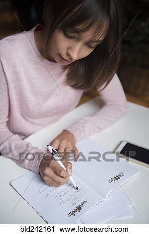 Stock Image - Mixed Race woman writing list in notepad. Fotosearch