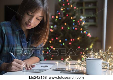 Stock Photo - Mixed Race woman writing on card near Christmas tree. Fotosearch