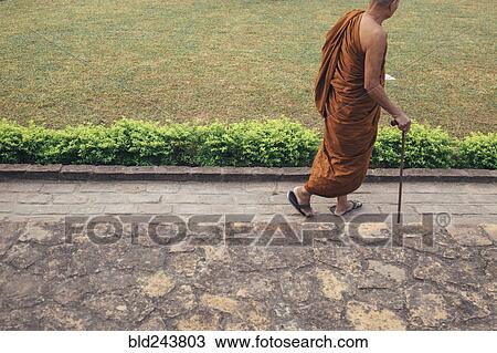 Stock Image - Monk walking with cane. Fotosearch