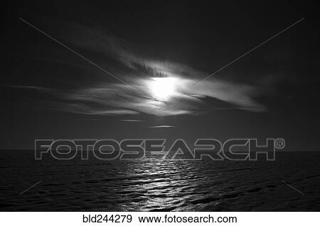 Stock Photo - Moon shining behind cloud over ocean. Fotosearch