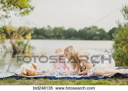 Stock Photography - Mother and daughter playing with stuffed animals on blanket near lake. Fotosearch