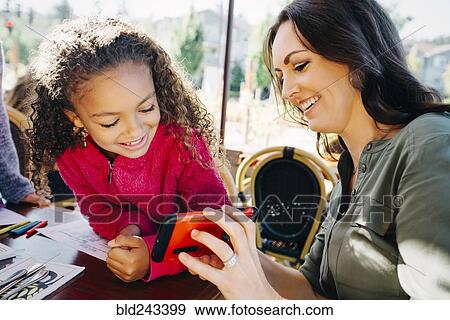 Stock Photo - Mother and daughter texting on cell phone in restaurant. Fotosearch