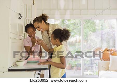 Stock Image - Mother and daughters decorating cake with icing. Fotosearch