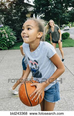 Stock Photo - Mother and daughters playing basketball in driveway. Fotosearch