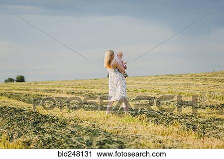 Stock Image - Mother carrying baby daughter in field. Fotosearch