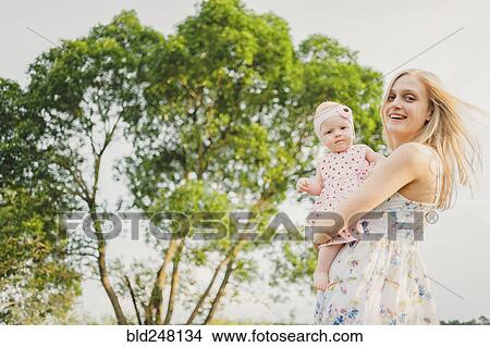 Picture - Mother carrying baby daughter near tree. Fotosearch
