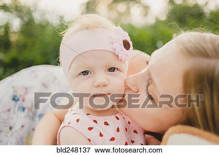 Stock Photo - Mother kissing baby daughter on cheek. Fotosearch