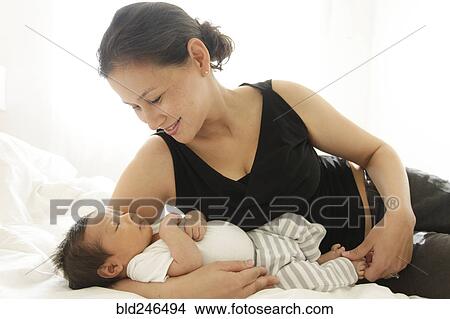 Picture - Mother laying on bed cradling sleeping baby son. Fotosearch