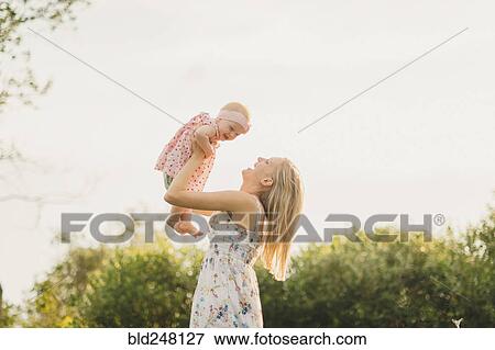 Stock Photo - Mother lifting baby daughter on sunny day. Fotosearch