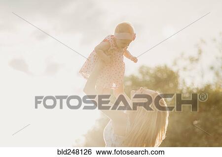 Mother lifting baby daughter on sunny day View Large Photo Image Stock Photograph - Mother lifting baby daughter on sunny day. Fotosearch