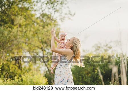 Stock Photo - Mother playing with baby daughter on sunny day. Fotosearch
