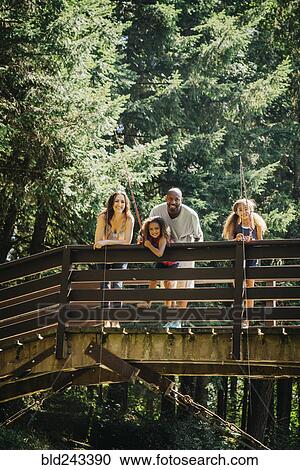 Stock Image - Multi-ethnic family fishing on bridge over river. Fotosearch
