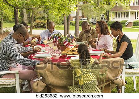 Stock Image - Multi-generation family praying at picnic table. Fotosearch