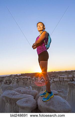 Stock Image - Native American woman standing on rock in desert. Fotosearch