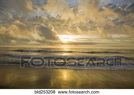 Stock Photo - Ocean waves on beach at sunset. Fotosearch