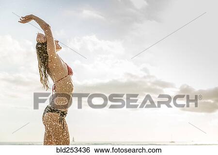 Stock Photograph - Ocean waves splashing on Caucasian woman wearing bikini. Fotosearch