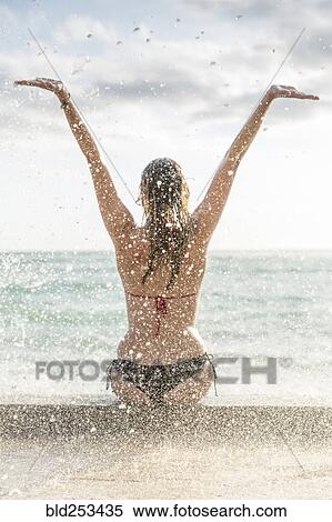 Stock Photography - Ocean waves splashing on Caucasian woman wearing bikini. Fotosearch