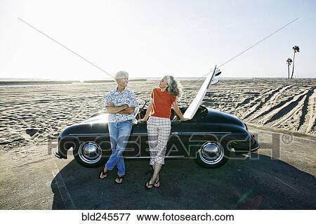 Older Caucasian couple leaning on convertible car with surfboard on beach View Large Photo Image Stock Photo - Older Caucasian couple leaning on convertible car with surfboard on beach. Fotosearch