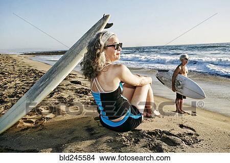 Picture - Older Caucasian couple on beach with surfboards. Fotosearch