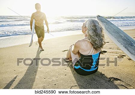 Stock Image - Older Caucasian couple on beach with surfboards. Fotosearch