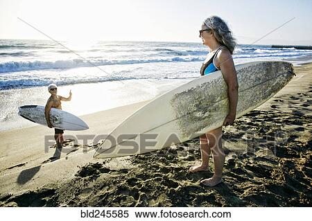 Stock Photography - Older Caucasian couple standing on beach with surfboards. Fotosearch