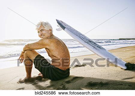 Older Caucasian man sitting on beach with surfboard View Large Photo Image Stock Photograph - Older Caucasian man sitting on beach with surfboard. Fotosearch