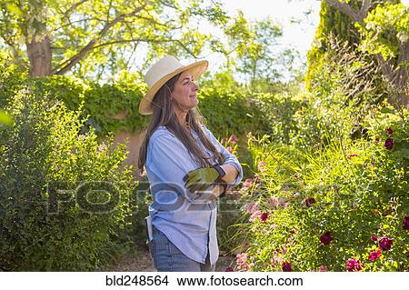 Picture - Older Caucasian woman admiring flowers in garden. Fotosearch