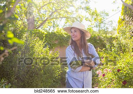 Stock Photography - Older Caucasian woman admiring flowers in garden. Fotosearch