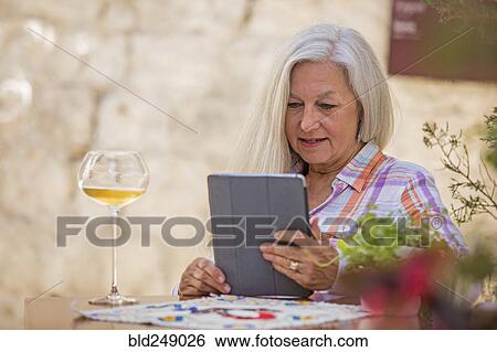 Older Caucasian woman drinking white wine and using digital tablet View Large Photo Image Stock Photograph - Older Caucasian woman drinking white wine and using digital tablet. Fotosearch