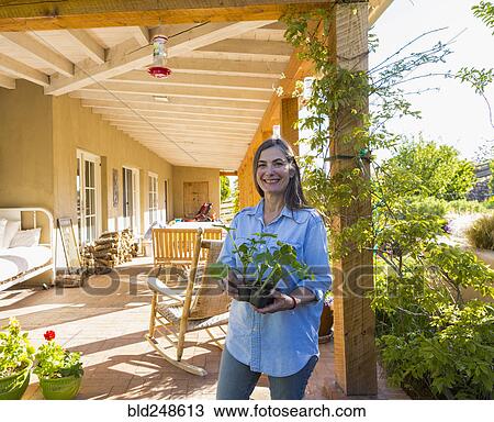 Stock Image - Older Caucasian woman holding seedlings on patio. Fotosearch