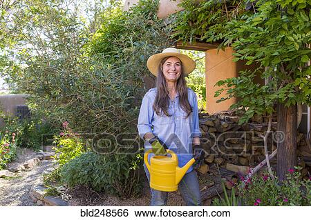 Stock Photograph - Older Caucasian woman holding water can in garden. Fotosearch
