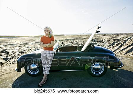 Older Caucasian woman leaning on convertible car with surfboard on beach View Large Photo Image Stock Photograph - Older Caucasian woman leaning on convertible car with surfboard on beach. Fotosearch