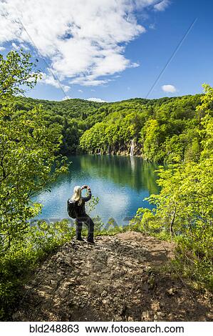 Stock Image - Older Caucasian woman photographing waterfall with cell phone. Fotosearch
